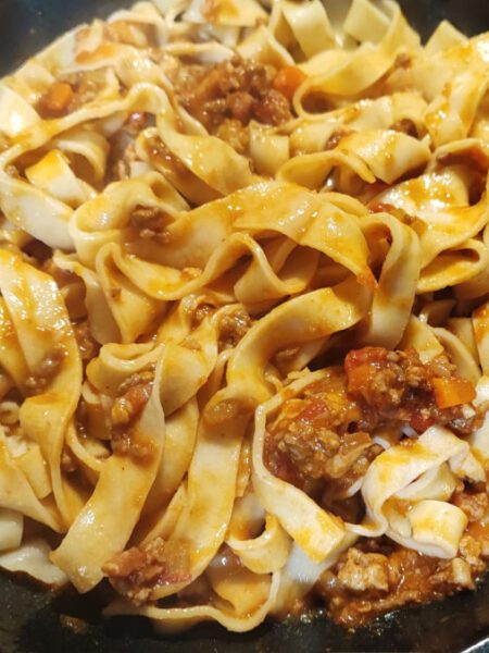 Tagliatelle being gently tossed with sauce in a frying pan