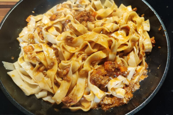 Tagliatelle being gently tossed with sauce in a frying pan
