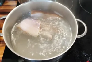 Ein ganzes Stück geräucherter Bauchspeck wird in einem Topf mit Wasser für die Brühe ausgekocht.