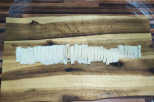 Rolled dough sheet being cut into tagliatelle strips with a sharp knife 2