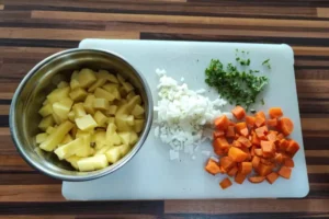 Vorbereitete Suppeneinlagen bestehend aus gewürfelten Kartoffeln, Möhren, Zwiebeln und frischer Petersilie auf einem Holzbrett.