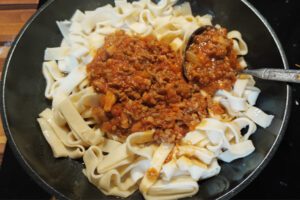 Tagliatelle being gently tossed with sauce in a frying pan