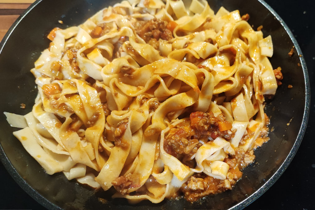 Tagliatelle being gently tossed with sauce in a frying pan