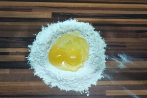 Mehlhügel mit Eiern in einer Mulde auf Holzarbeitsfläche