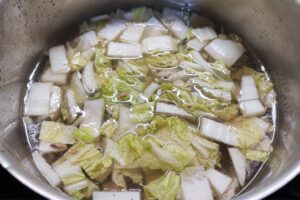 Adding roughly chopped napa cabbage (Baechu / 배추) to the pot.