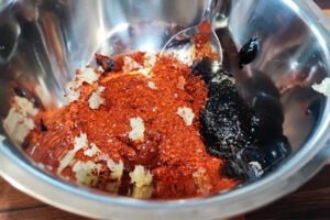 Combining gochujang, gochugaru, soy sauce, jocheong, chunjang and garlic in a bowl.